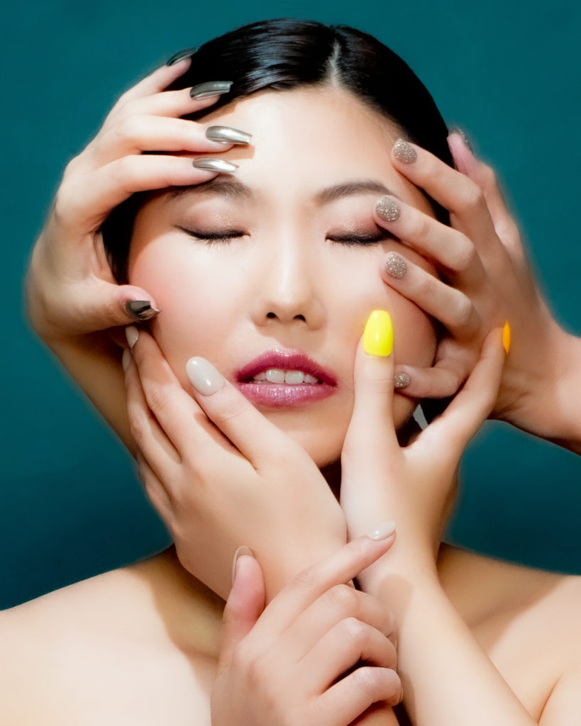 女性の顔の周りにネイルチップをつけた手がたくさんある