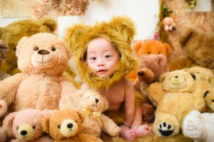 たくさんのクマの縫いぐるみの中、赤ちゃんがクマの着ぐるみを着ている