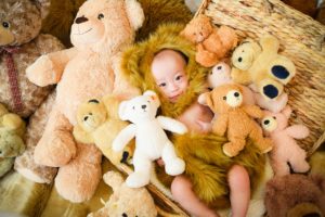 たくさんのクマの縫いぐるみの中、赤ちゃんがクマの着ぐるみを着ている