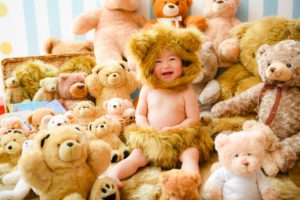 たくさんのクマの縫いぐるみの中、赤ちゃんがクマの着ぐるみを着ている