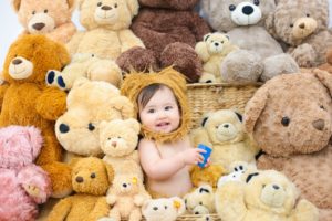 たくさんのクマの縫いぐるみの中、赤ちゃんがクマの着ぐるみを着ている