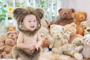 たくさんのクマの縫いぐるみの中、赤ちゃんがクマの着ぐるみを着ている