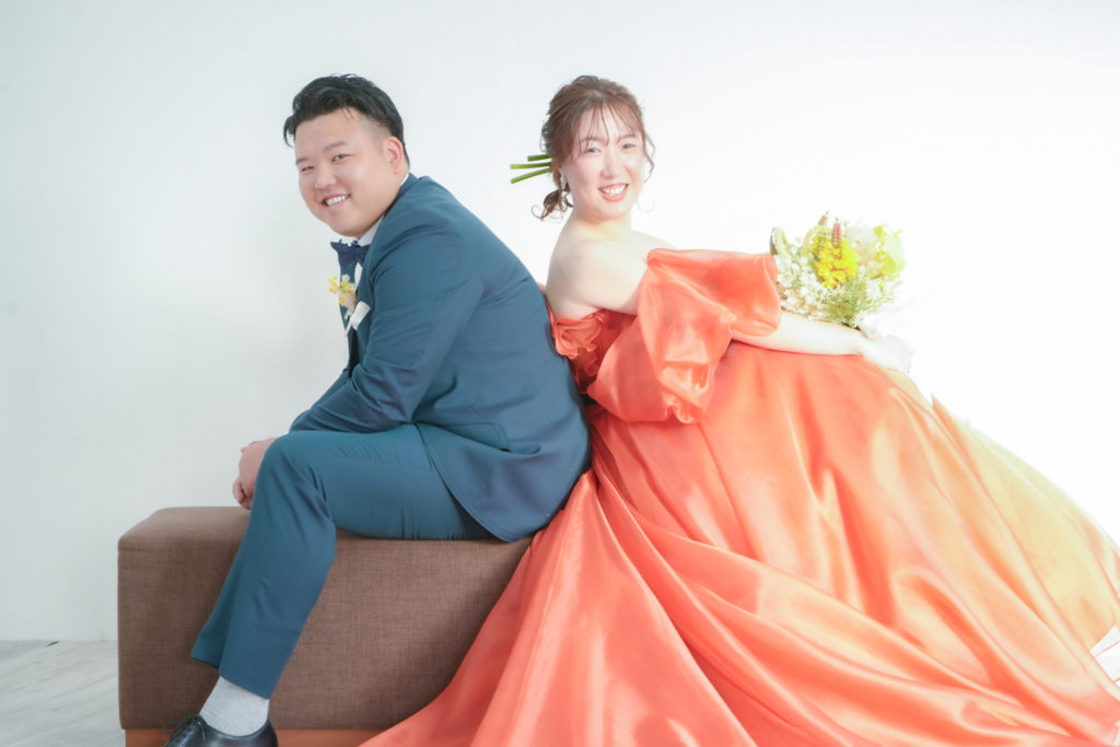 オレンジ色のドレスを着た新婦とネイビーのタキシードを着た男性