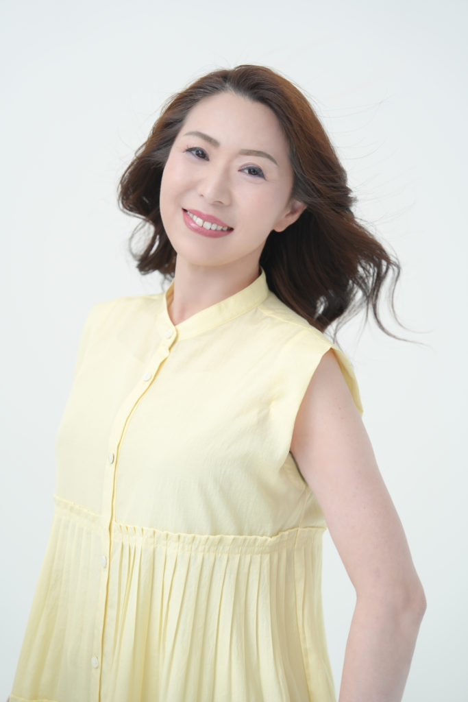 黄色いワンピースの 女性が笑顔で立っている
